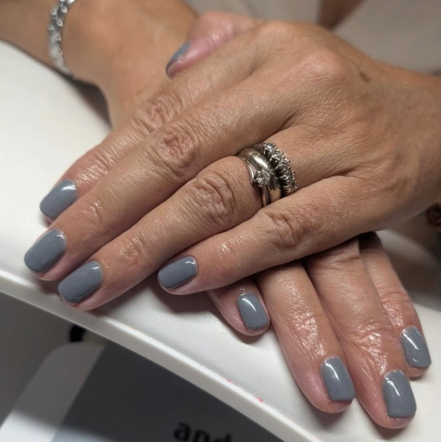 Close-up of hands with grey nail polish on a white surface.
