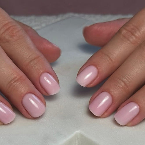 Close-up of two hands with pink nail polish on a neutral background
