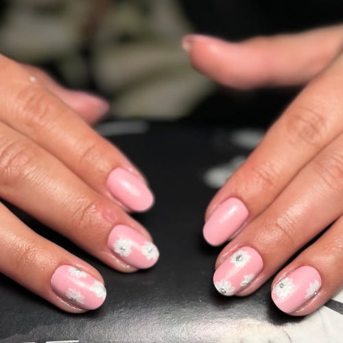 Close-up of two hands with pink nail polish and silver glitter on a dark surface