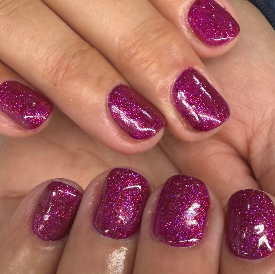 Close-up of a hand with glittery pink nail polish on a neutral background