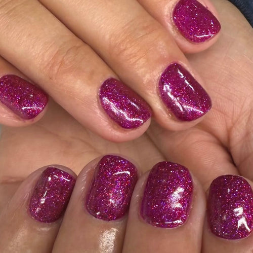 Close-up of a hand with glittery pink nail polish on a neutral background
