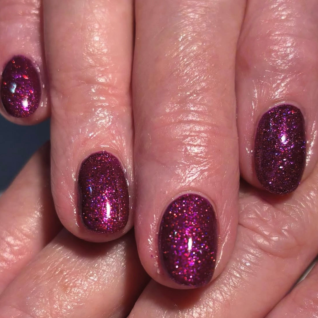 Close-up of a hand with pink glittery nail polish on a neutral background