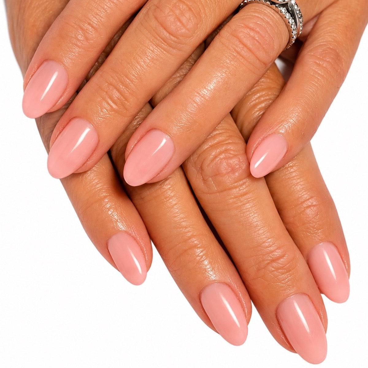 A close-up of two hands with neatly manicured, glossy almond-shaped nails in a soft dusty pink shade, with a silver ring visible on one finger against a plain white background.