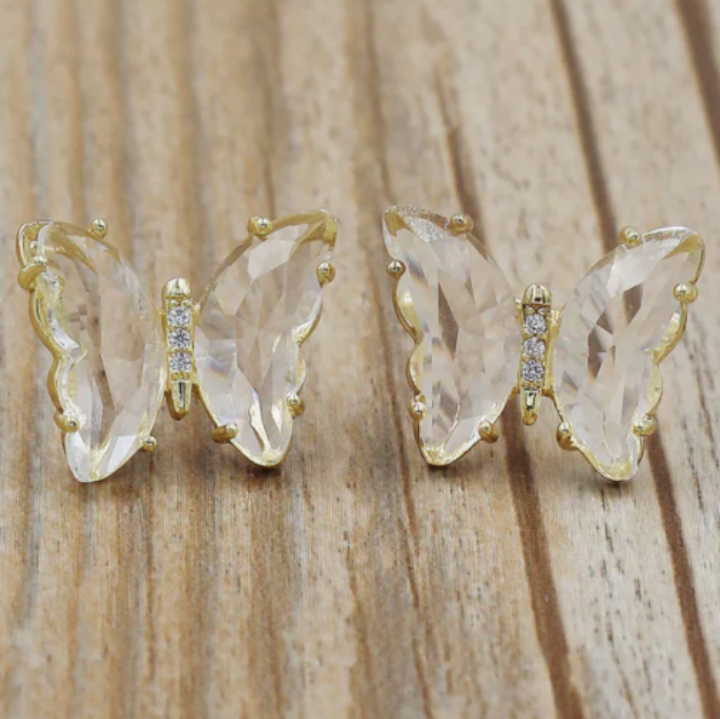 Pair of butterfly-shaped clear and gold nail  gemstones on a wooden surface