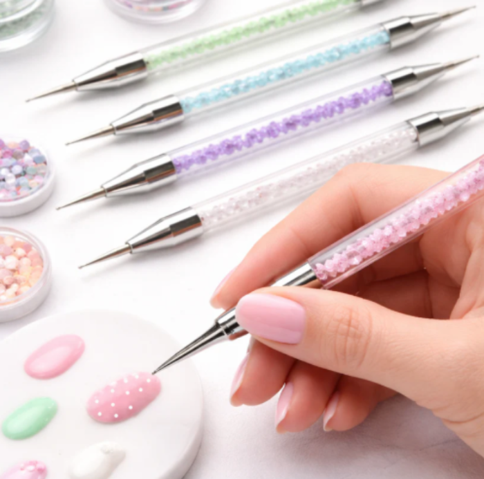 Set of decorative nail art tools with a hand holding one tool, on a light background.