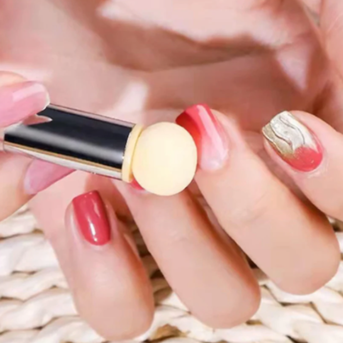 Hand holding a blender nail sponge pen with red nail polish on a blurred background