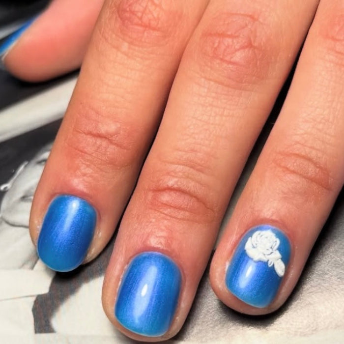 Close-up of a hand with blue nail polish and a white flower design on a gray background
