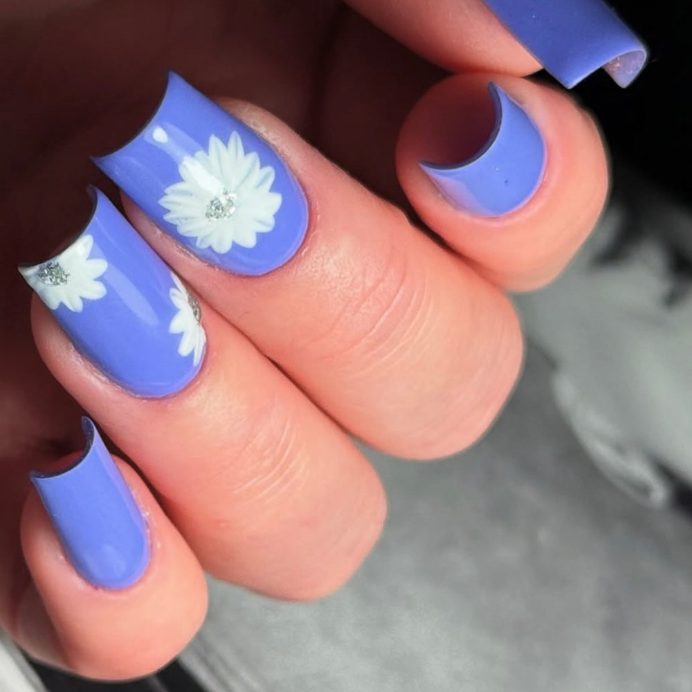 Close up of a hand with nail art showing white flowers on a purply-blue gel polish 