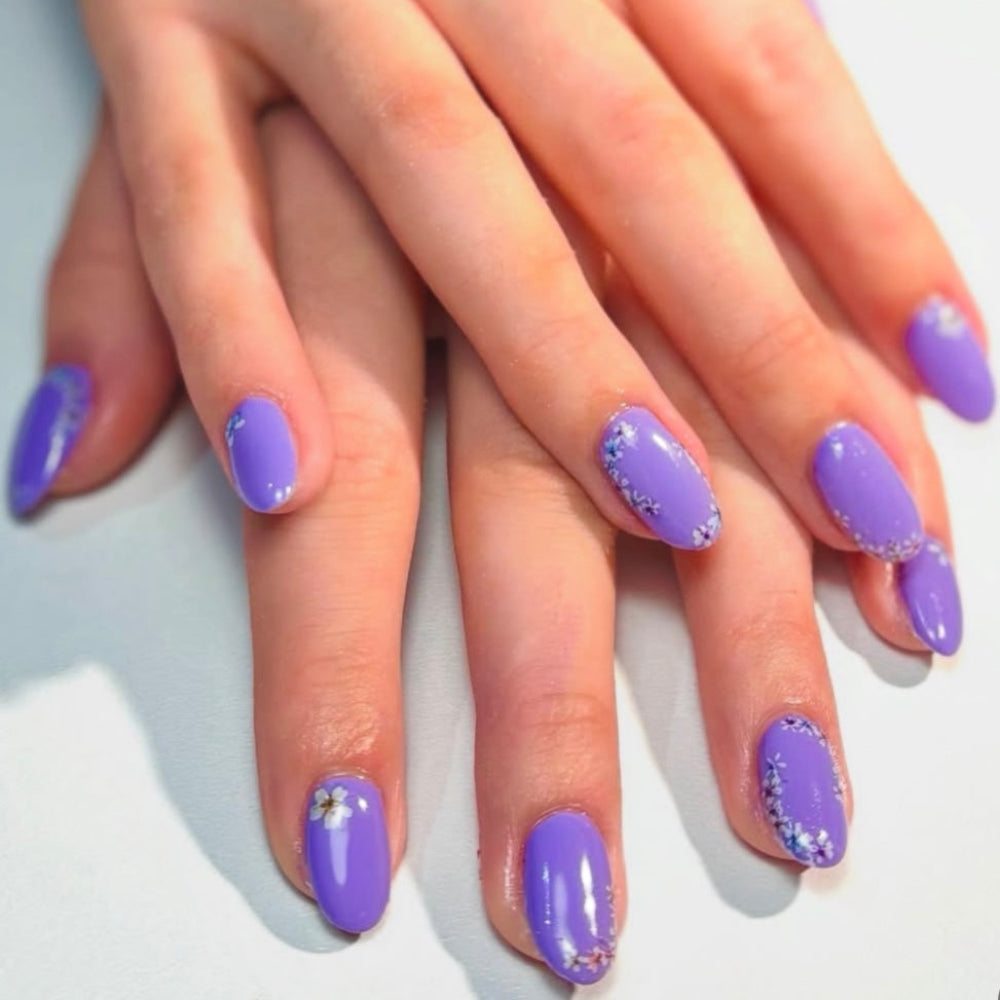 Close up of hands showing nails with a purple gel polish and flowery nail art 