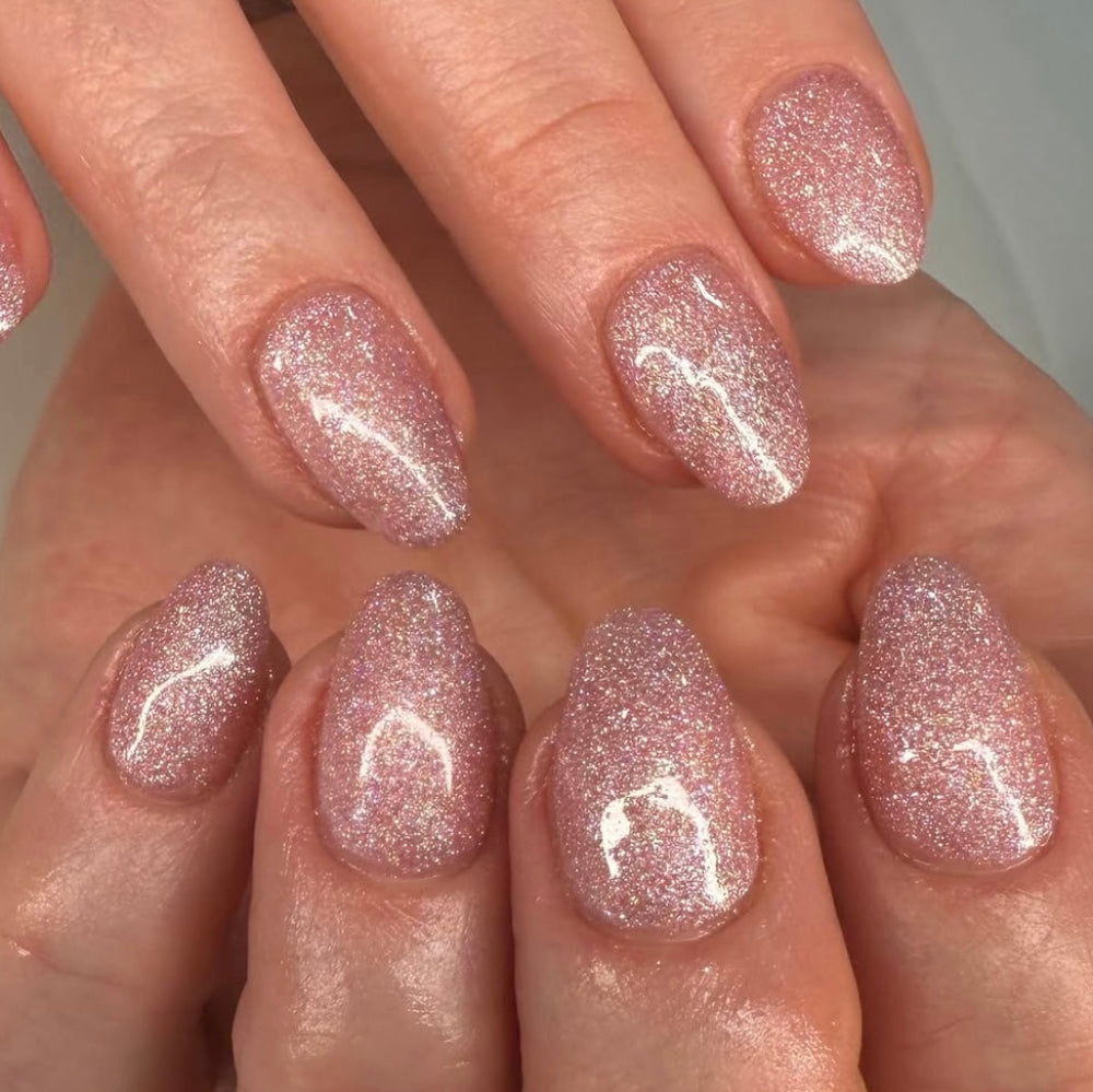 Close-up of hands with pink glittery nail polish on a neutral background