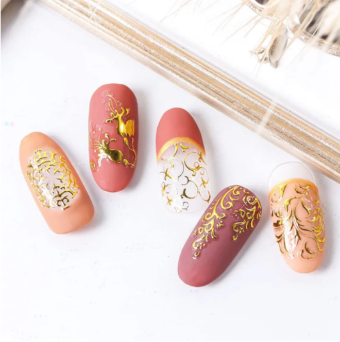 Nail art with gold and white designs on pink and beige nails.