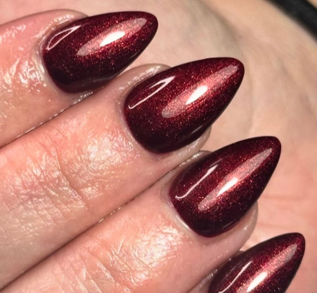 Close-up of a hand with dark red glittery nail polish on a neutral background