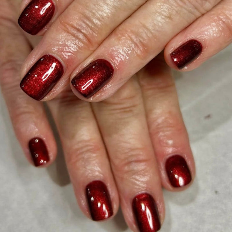 Close-up of a hand with red glittery nail polish on a neutral background