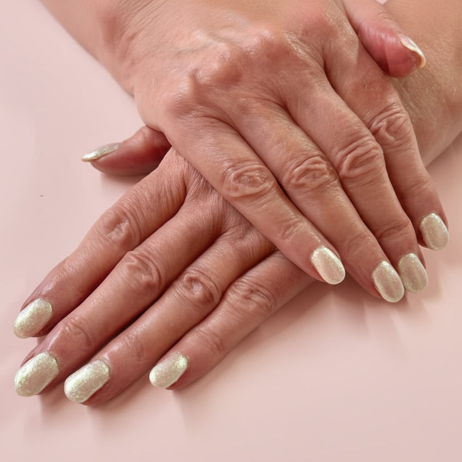 Close-up of hands with glittery nail polish on a pink background