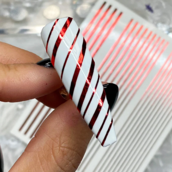 Red and white striped nail art swatch held between fingers with a blurred background