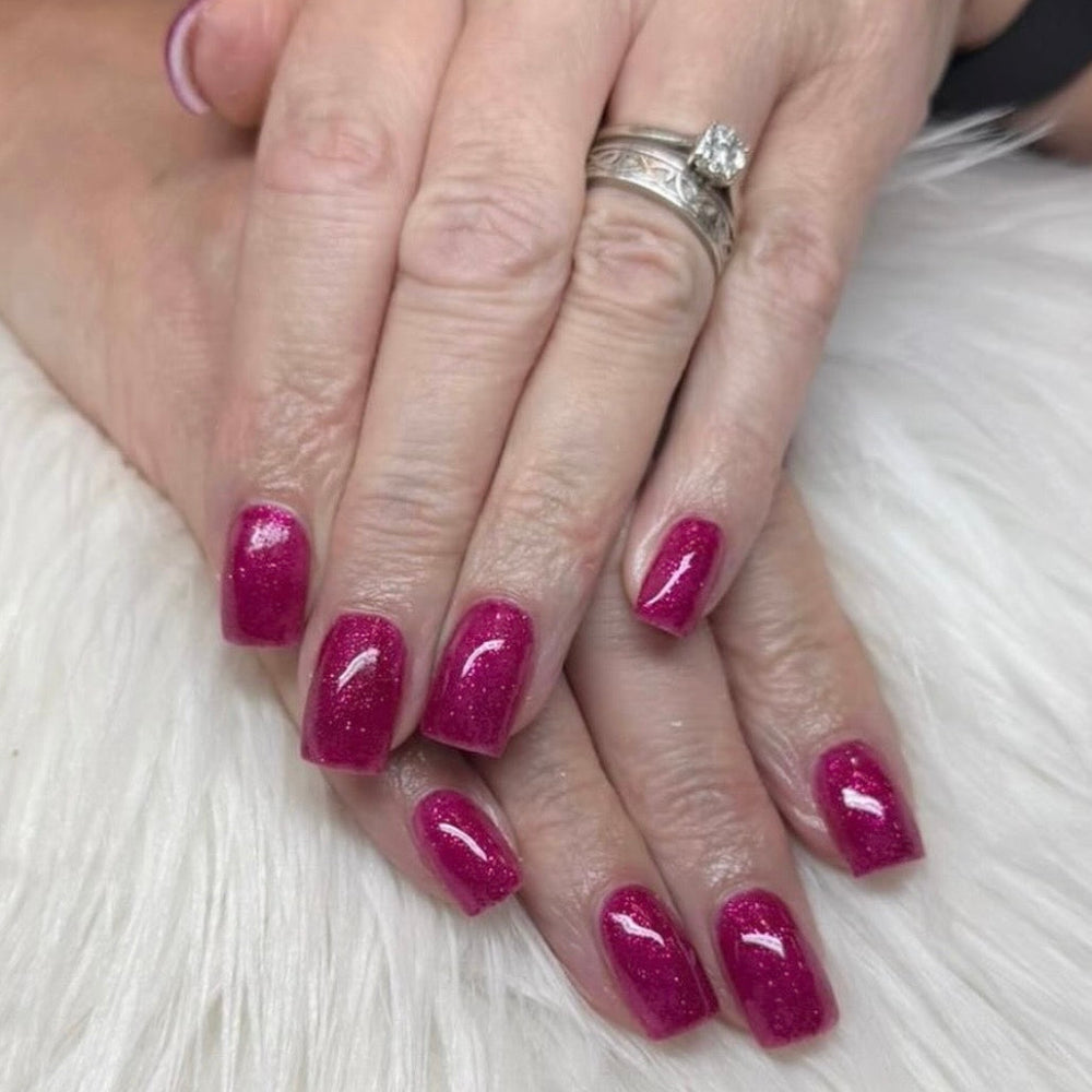 Hands with nails painted with a glittery pink gel polish on a light background 