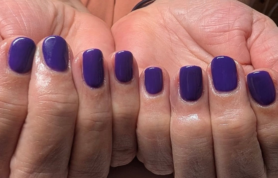 Close-up of hands with purple nail polish on a neutral background