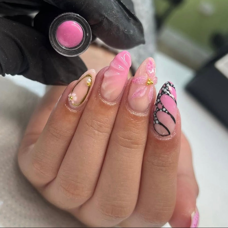 Hand with pink nail polish and decorative design, holding a pink nail polish bottle.