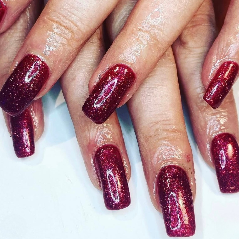 Close-up of hands with red glittery nail polish on a white background