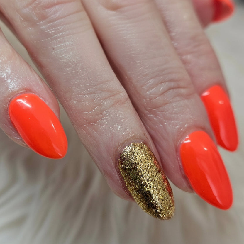 Hand with orange and gold glitter nail design, featuring a brand logo overlay.