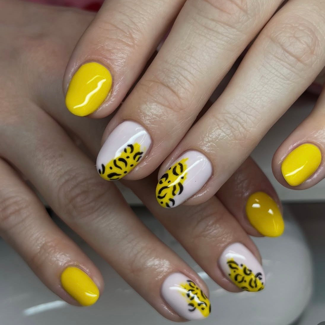 Close-up of hands with yellow and white nail design on a neutral background