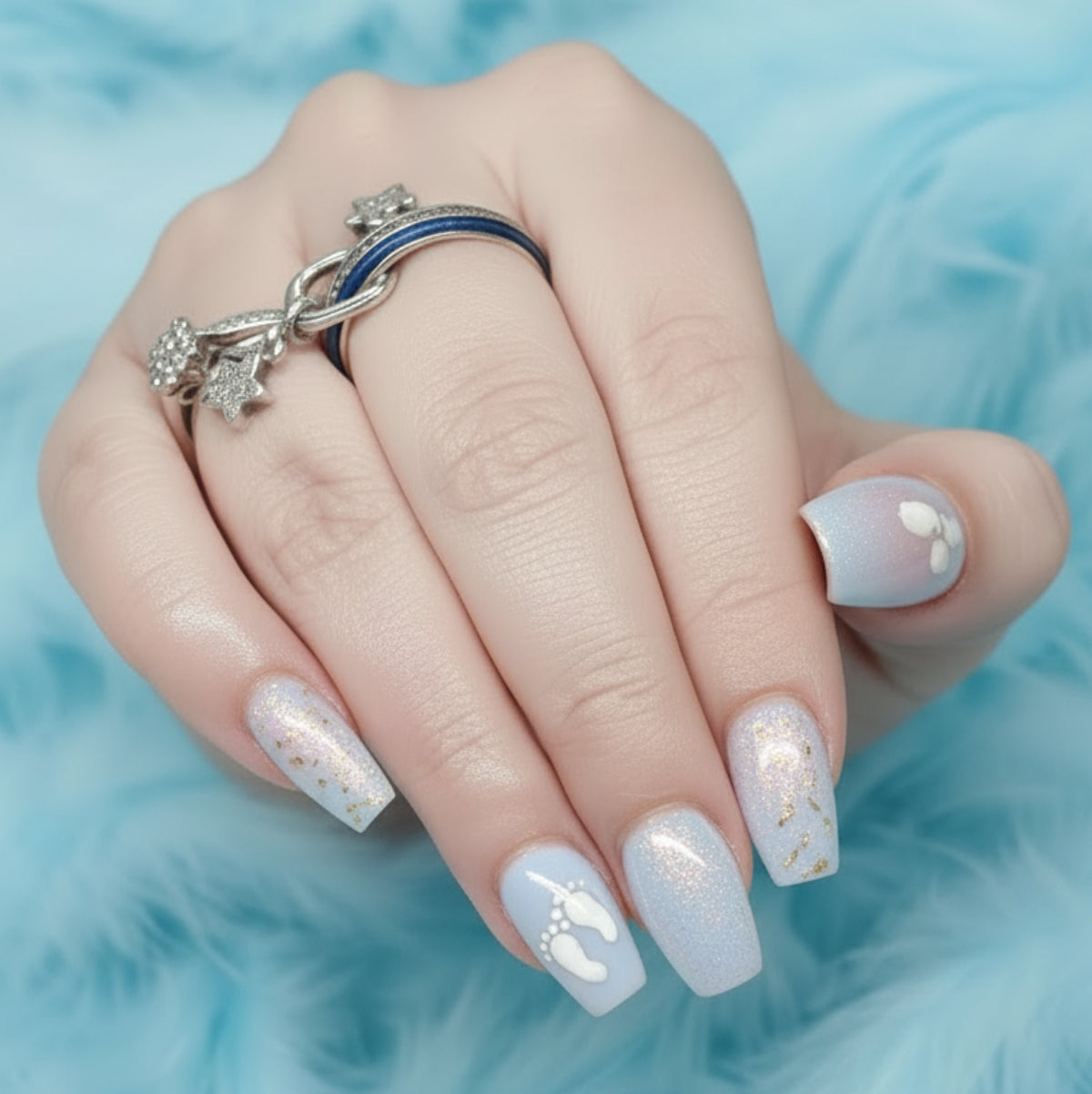 A nail set with a pale blue design with baby footprints on a blue feathery background