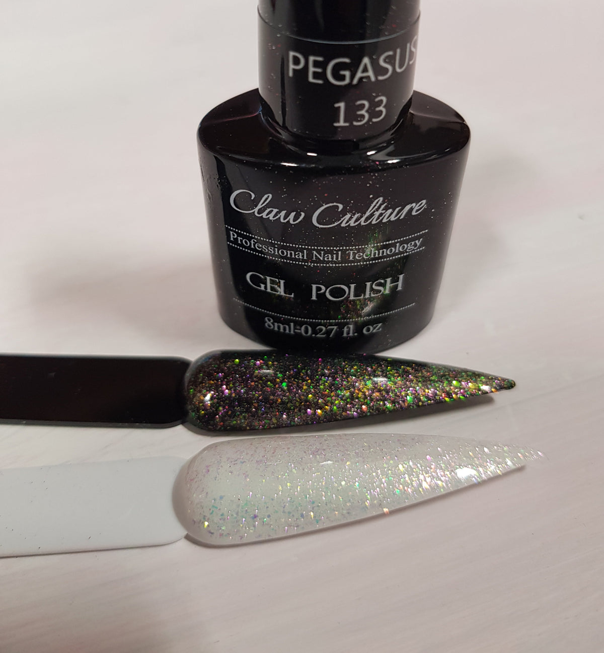 A bottle of Claw Culture Pegasus 133 gel polish with two nail swatches displayed in front on a light surface. The top swatch shows a dark glittery green base with multicolor holographic flakes, and the bottom swatch shows a sheer white base with fine silver holographic glitter.